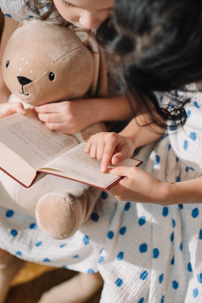 Two girls reading a book together, holding a plush bunny, promoting literacy and family bonding.